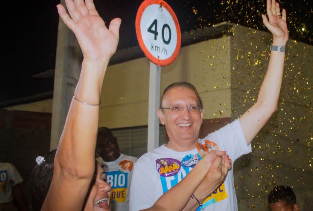 Fábio Henrique sorri com os braços levantados, cercado por apoiadores em comemoração de campanha à noite